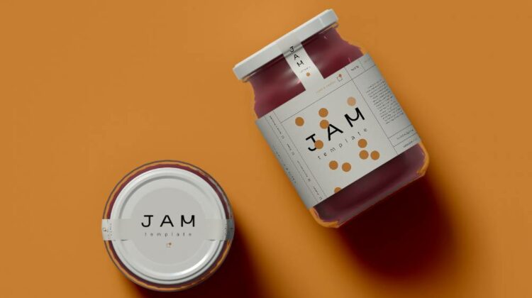 Two jam jars, one on its side and the other standing up, displaying a neat packaging label on a bright orange background.
